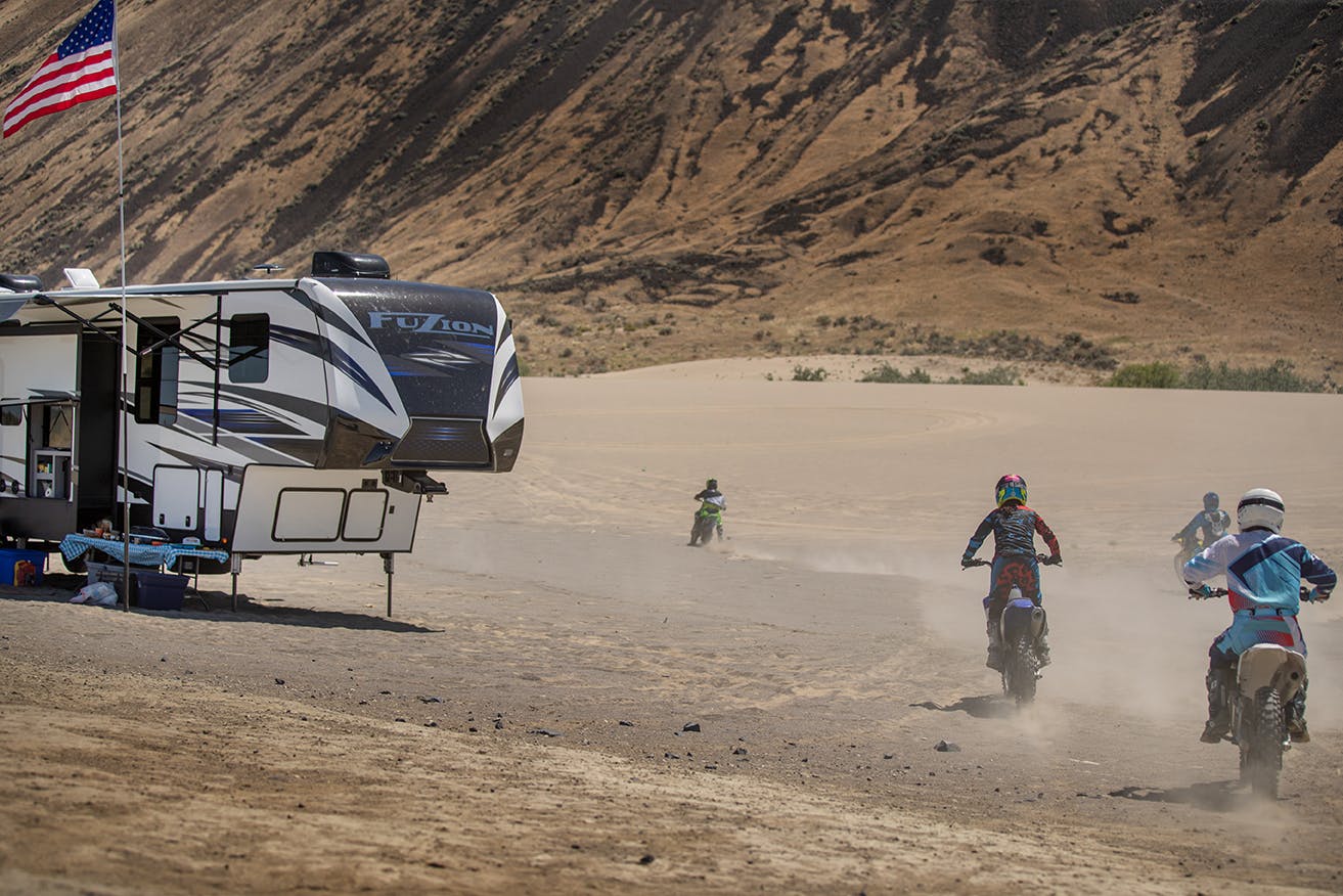 Children ride dirt bikes in the desert near a Keystone Toy Hauler Fifth Wheel