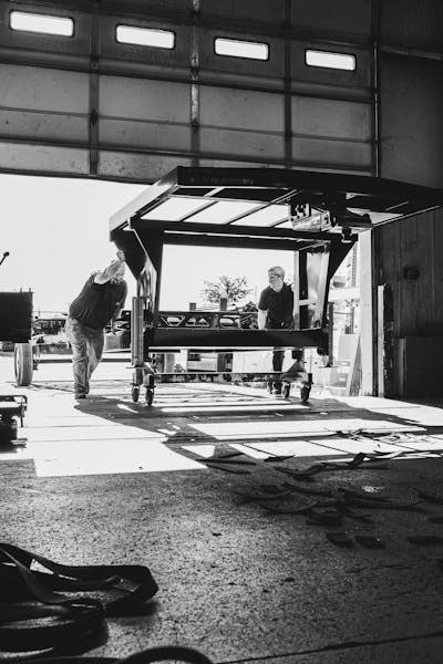 Two Keystone RV manufacturing team members rolling a fifth wheel RV chassis into the plant.