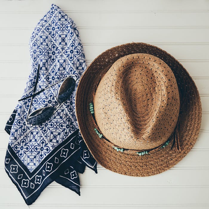 Straw hat, scarf and sunglass hanging on white beadboard wall.