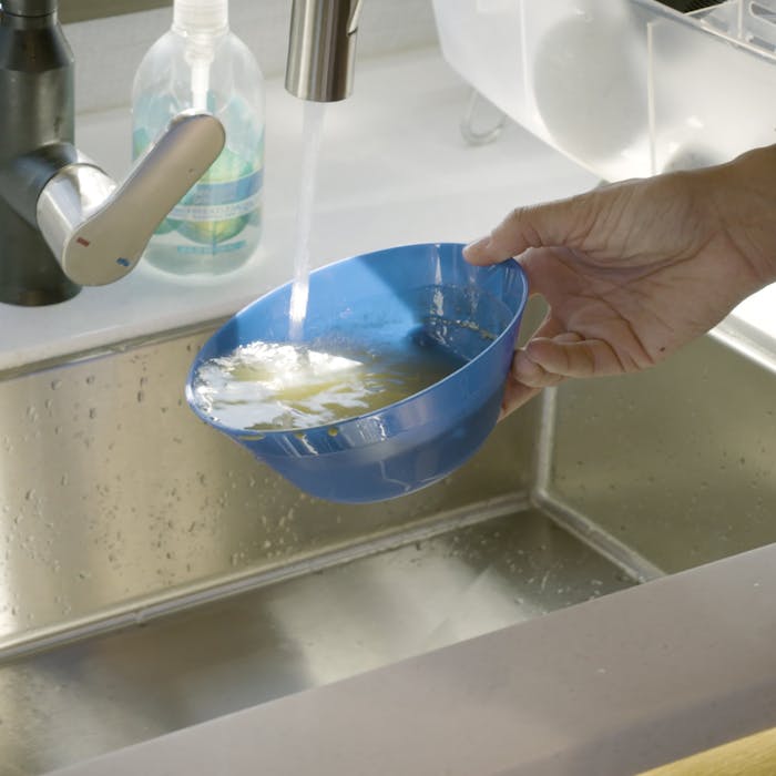 Hand holding blue bowl underneath tap in stainless steel sink.