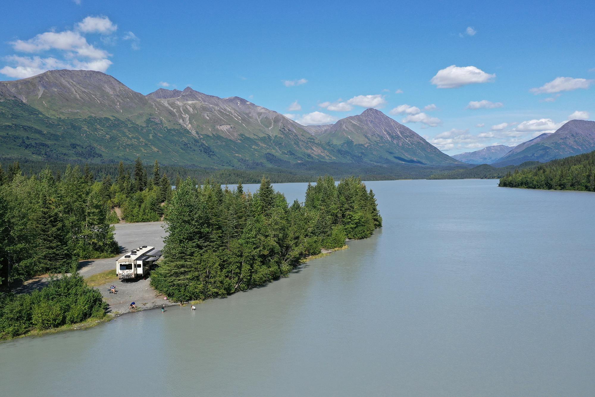 A fifth wheel parked on the side of a fjord with mountains in the background